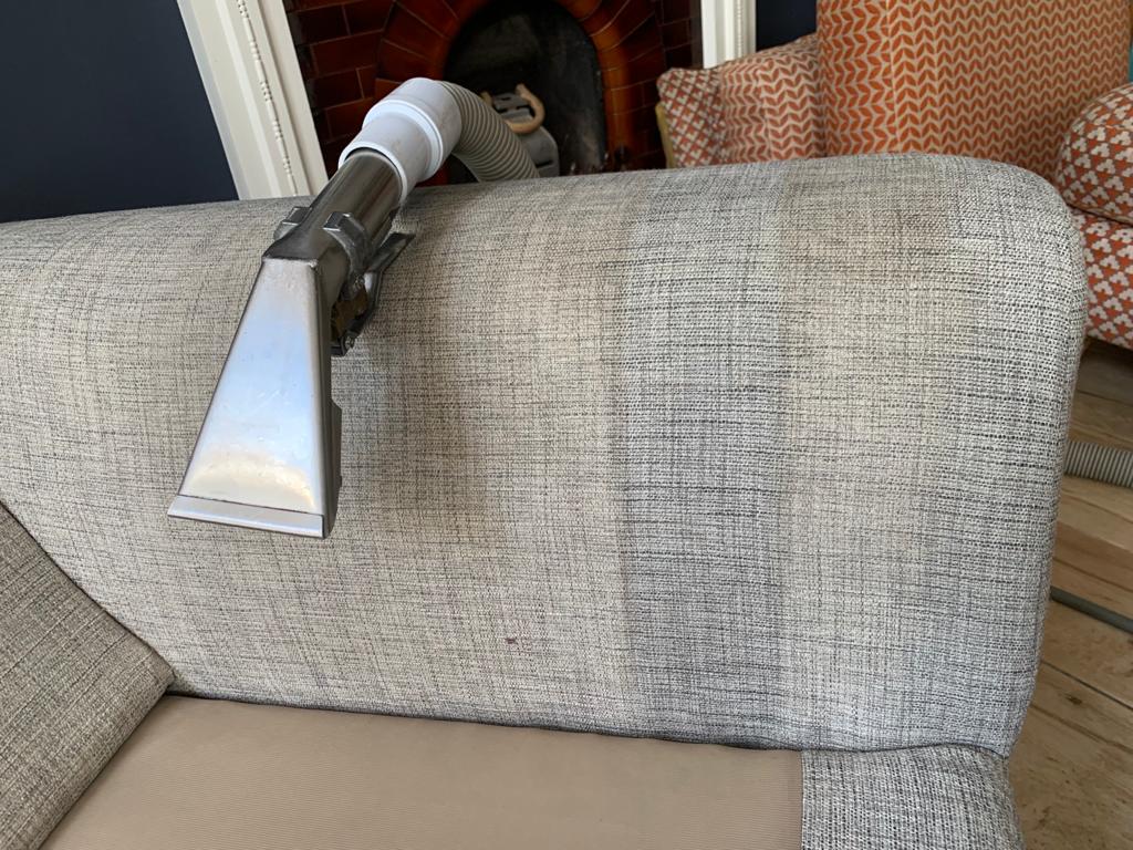 This is a photo of an arm of beige sofa that shows a test patch that has been steam cleaned. The steam cleaning machine is also showing in the photo works carried out by Ruislip Carpet Cleaning Solutions