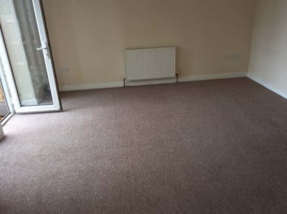 This is a photo of a living room after it has been cleaned. The room is empty and has a brown carpet that has been steam cleaned works carried out by Ruislip Carpet Cleaning Solutions